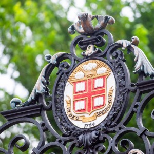 Brown University crest on an entry gate with green trees in the background.